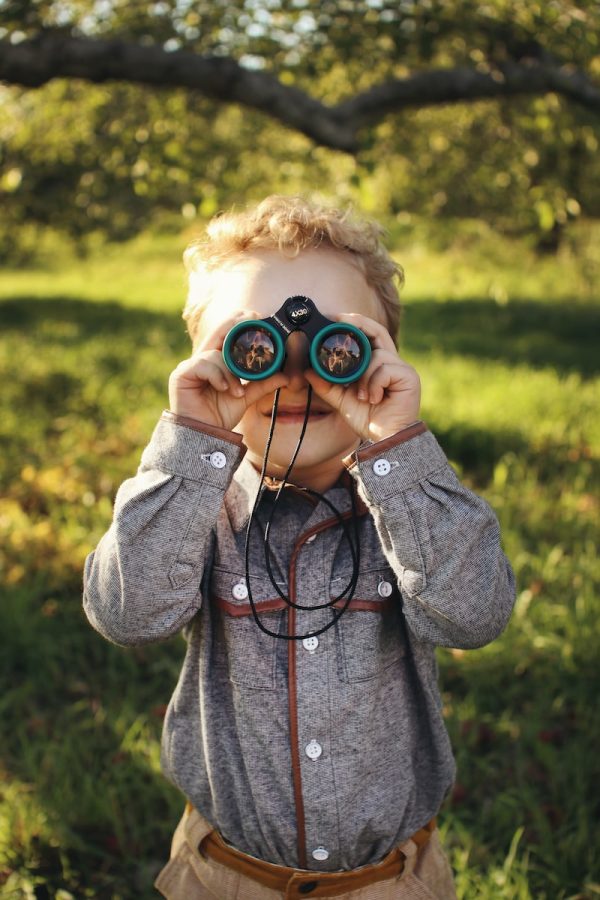 child standing while using green binoculars